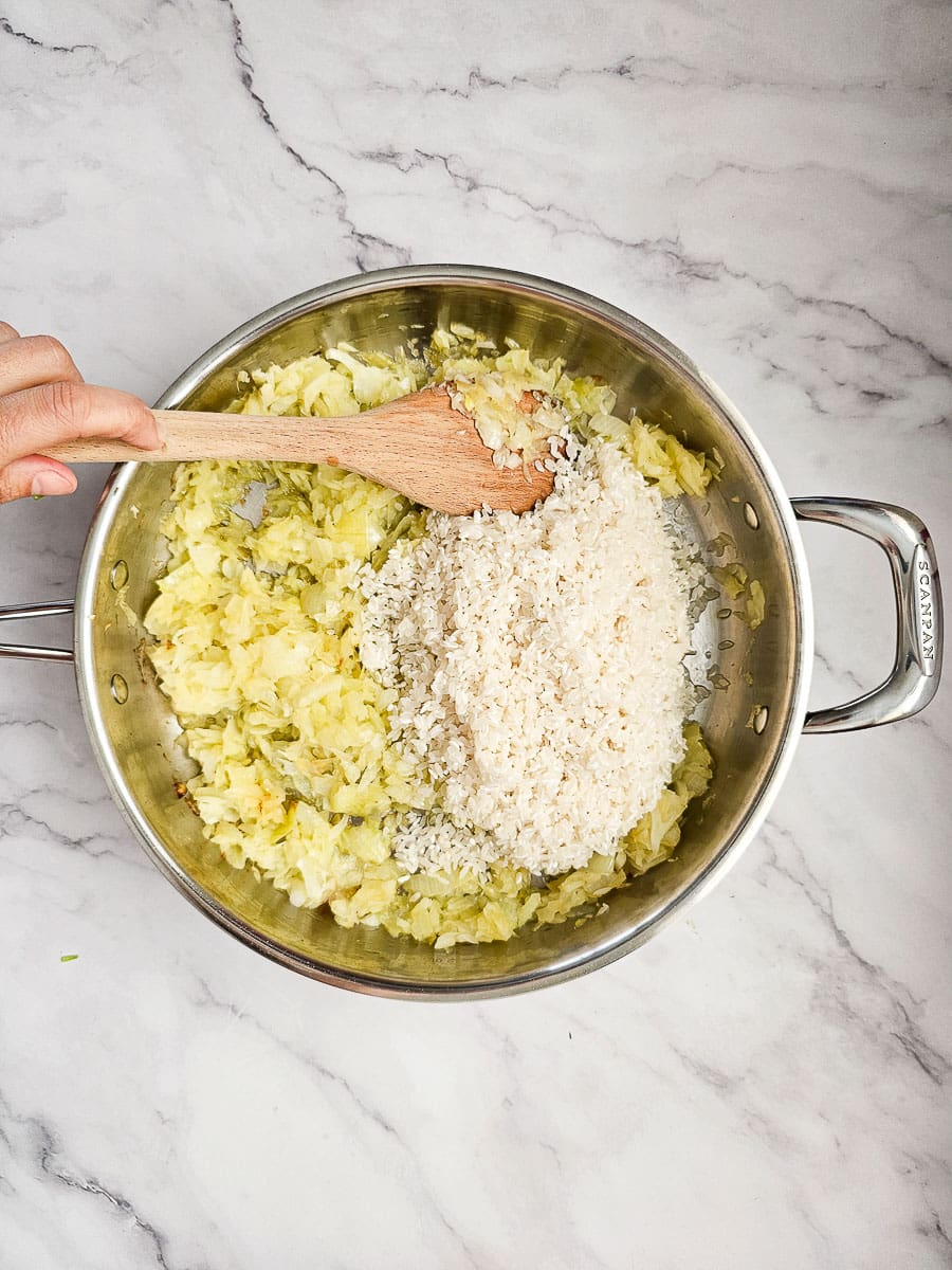 adding rice to sauteed onions in frying pan