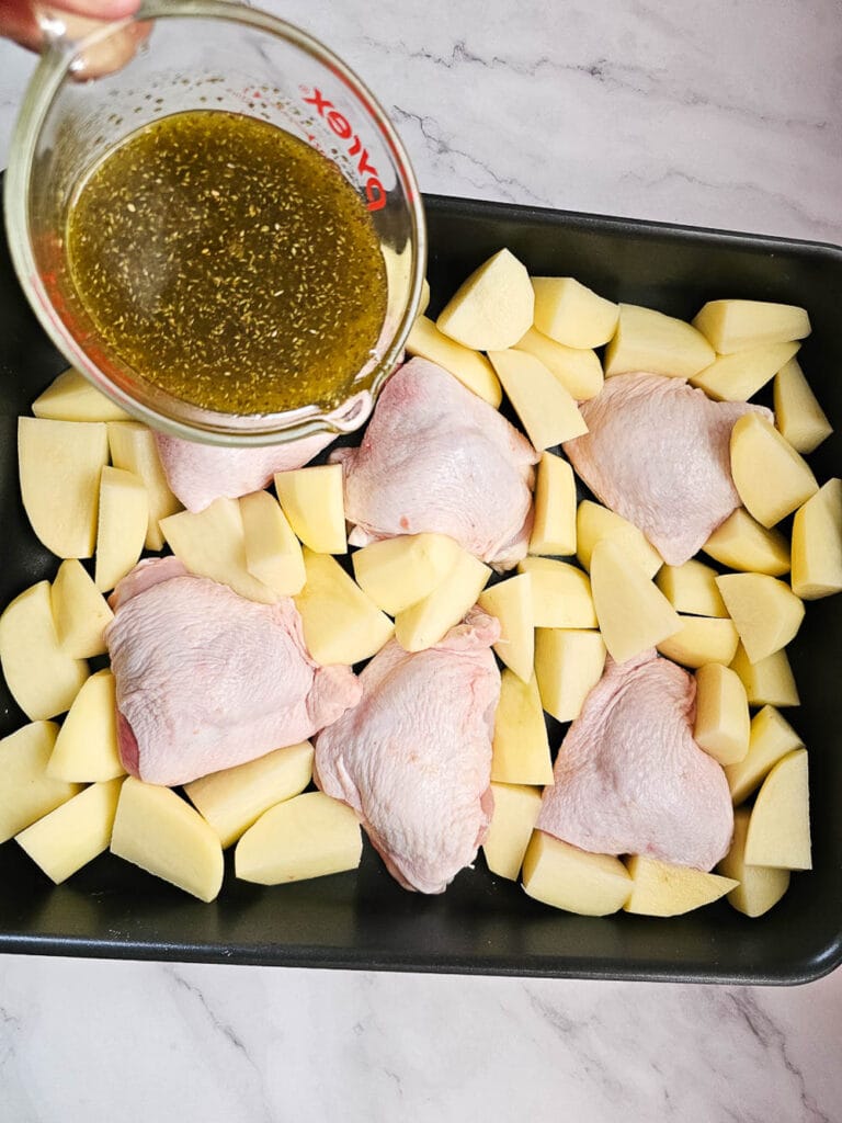 Adding olive oil, oregano and lemon juice to Greek Lemon Roasted Chicken and Potatoes in a baking tray