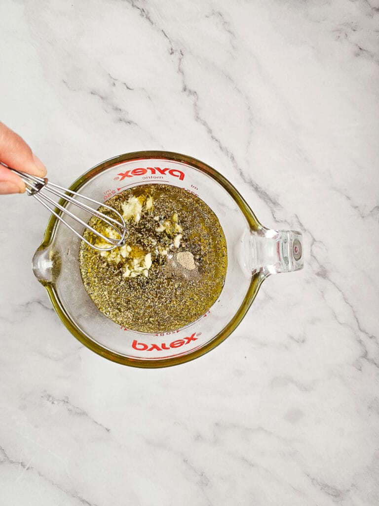 whisking olive oil, lemon juice, garlic and oregano marinade in jug