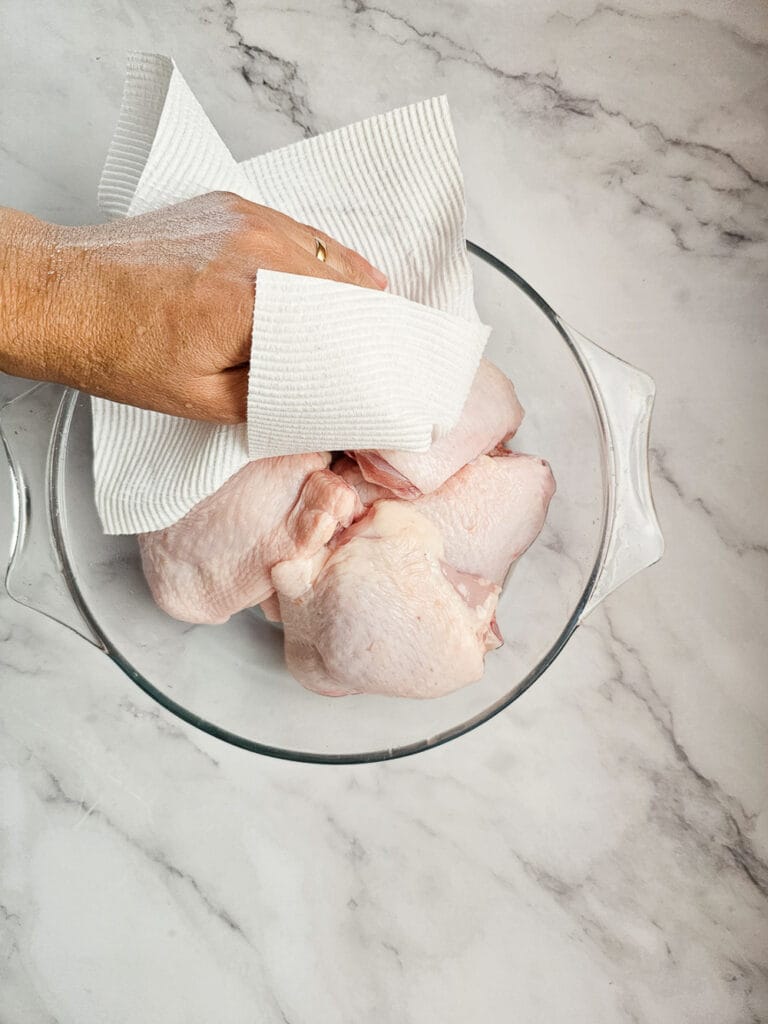 patting raw chicken thighs in a bowl
