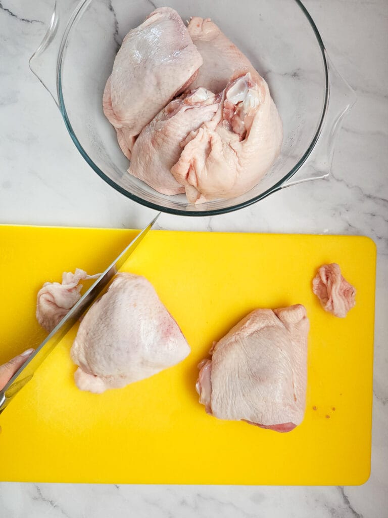 trimming fat off raw chicken thighs on yellow chopping board