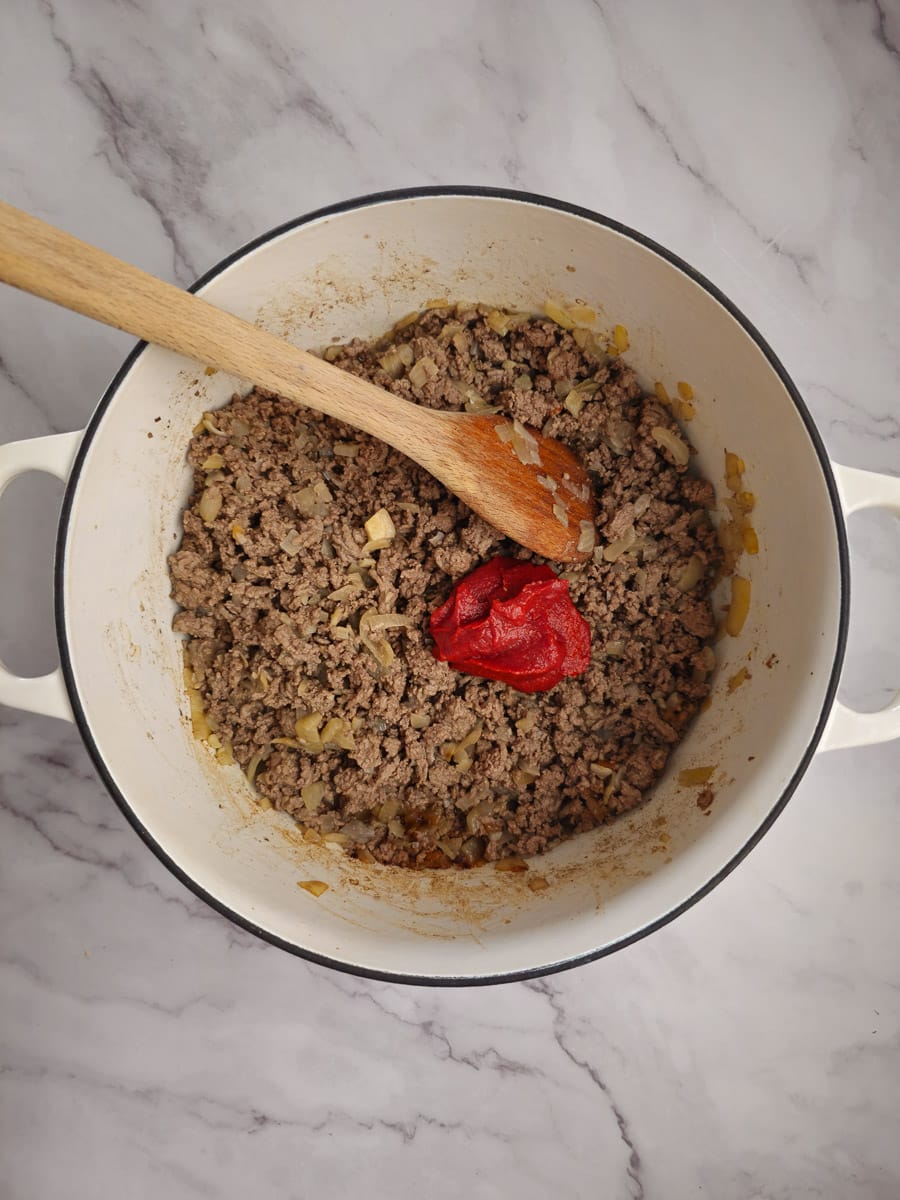 adding tomato paste to mince in pot