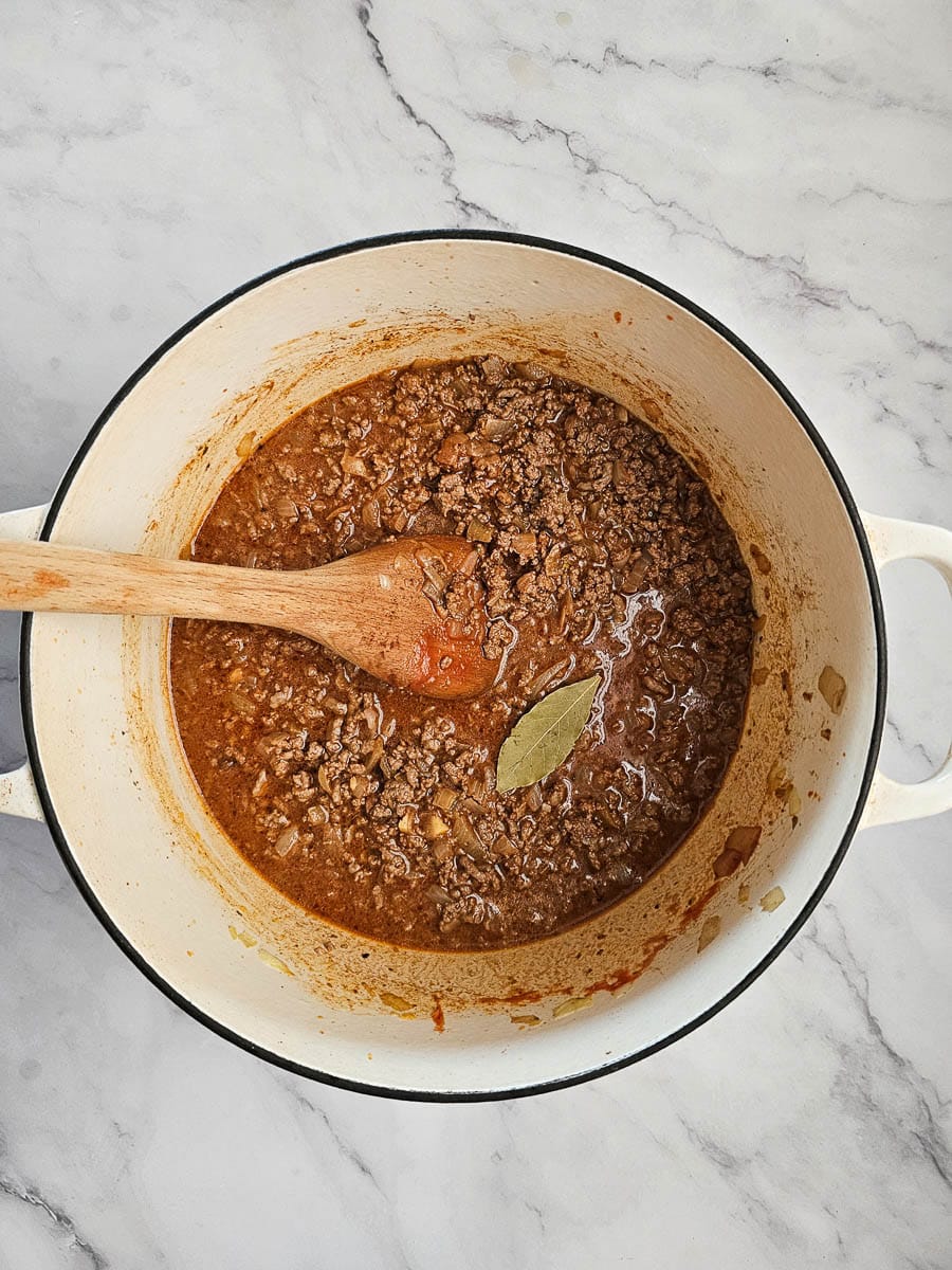adding bay leaf to meat sauce in dutch oven