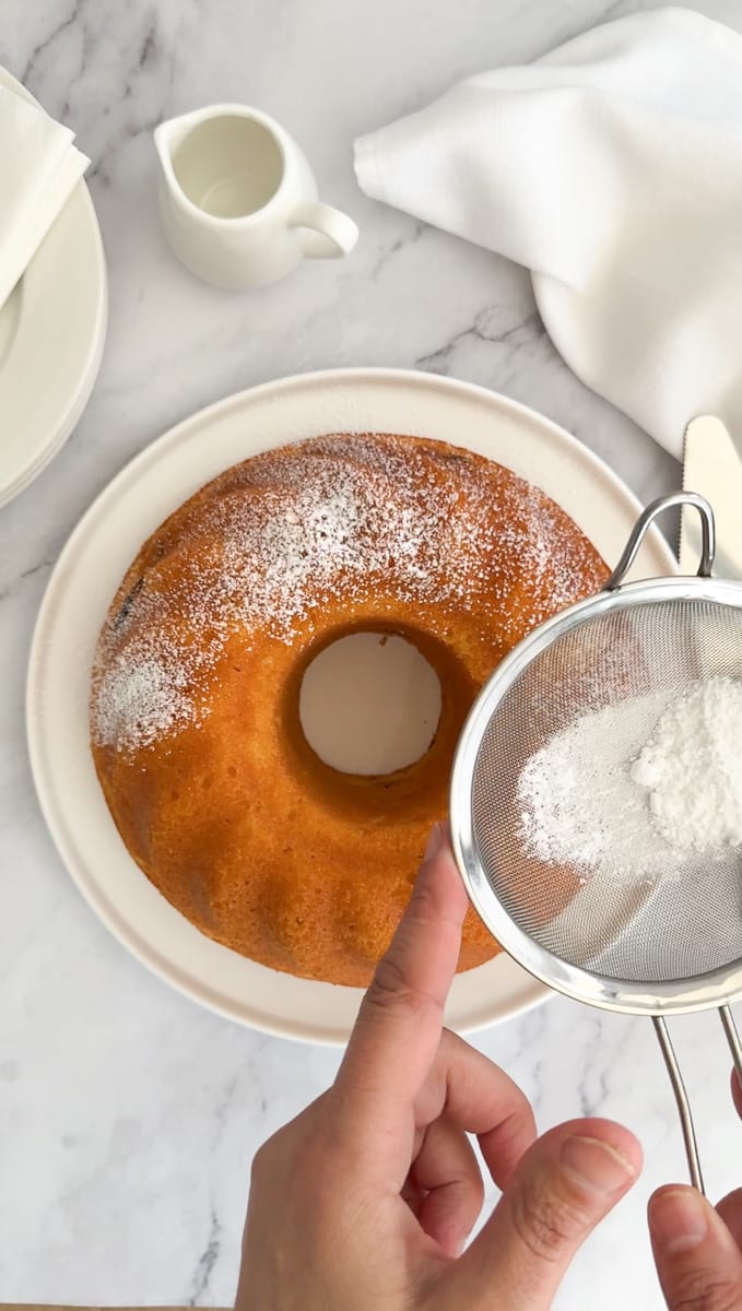 dusting yoghurt cake with icing sugar on a plate